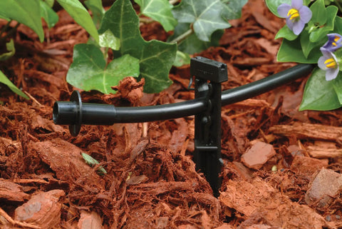 Close-up of Patio Drip Irrigation Kit With Faucet Connection, 42-Piece Set, one-quarter inch tubing in garden mulch with plants.