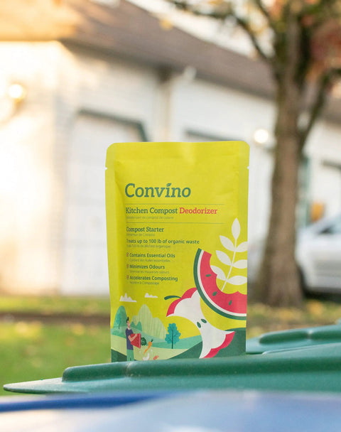 Front view of a yellow compost starter and odor reducer pack on a bin outdoors, featuring garden iconography.