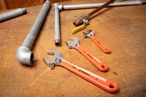 Three Piece Adjustable Cushion Grip Wrench Set With 6 Inch, 8 Inch And 10 Inch Jaw Wrenches on wooden table with pipes