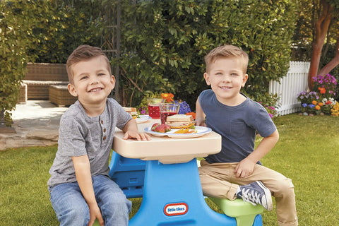 Two boys sitting at a Six Seat Kids Picnic Table With Umbrella Multi Color Outdoor Play Table With Center Cup Holders And Crayon Tray