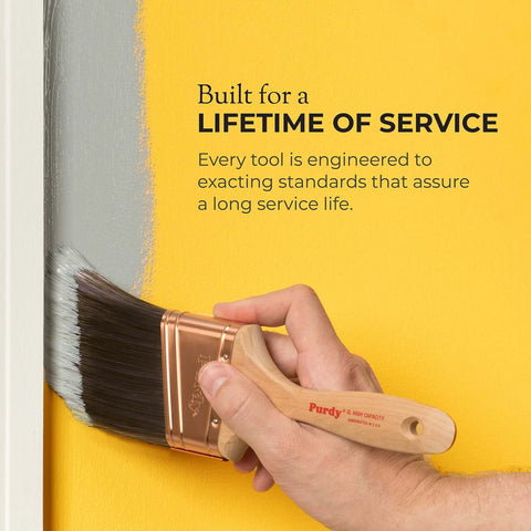 Hand holding a Purdy paintbrush applying gray paint on yellow wall, emphasizing durability and long service life.