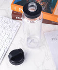 Clear water bottle on desk with black lid detached, showcasing 4 Pack Silicone Gasket Replacements For Yonder Water Bottles 20 Oz 25 Oz 34 Oz And 50 Oz Leak Proof O Ring Seals Silicone Sealing Rings Tumbler Lid Replacement Parts BPA Free Includes Removal Hook