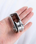 Person holding dual-bearing cable pulley wheel set for rope systems, wall or ceiling mounted, stainless steel construction