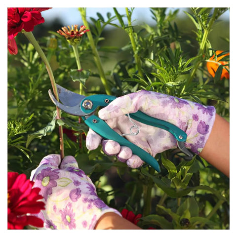 Hands wearing floral gloves using garden scissors, surrounded by plants with red and orange flowers in the background.