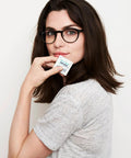 Woman holding Pre-Moistened Lens Wipes For Eyeglasses Individually Wrapped Streak Free pack next to her face.
