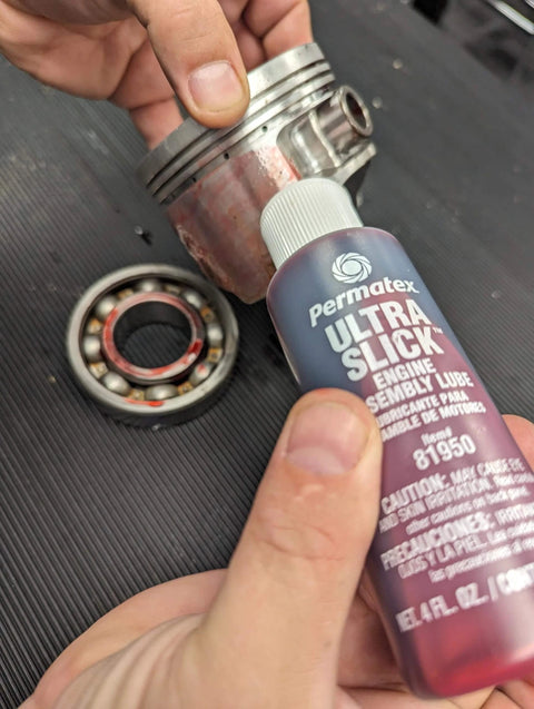 Permatex 81950 Ultra Slick Engine Assembly Lube, 4 oz., Red bottle next to metal engine bearings on a workbench.