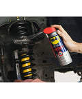 Applying WD-40 Specialist Penetrant with Smart Straw to metal car parts, showing 11 oz. can in use for fast-acting corrosion removal.